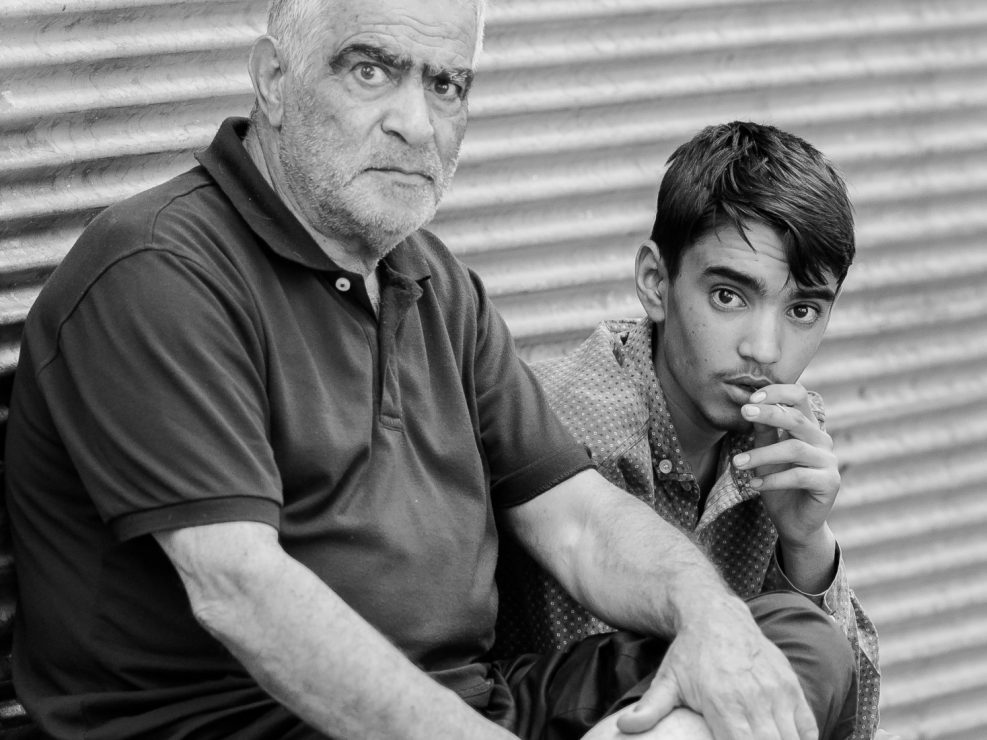 Grandfather and grandson sitting outside their shop, Iran