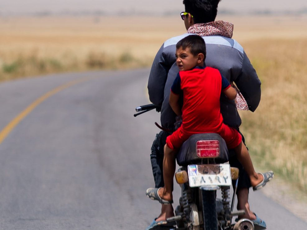 Child riding on the back of a motorbike without a helmet, Iran