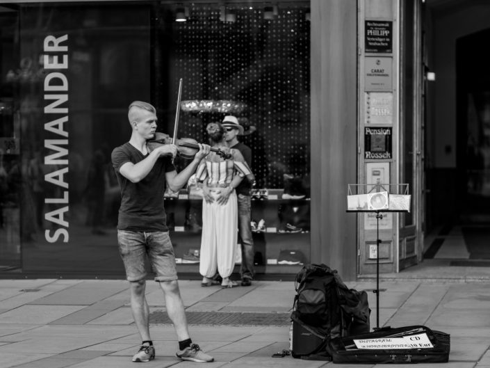 Street musician playing violin, couple background hugging